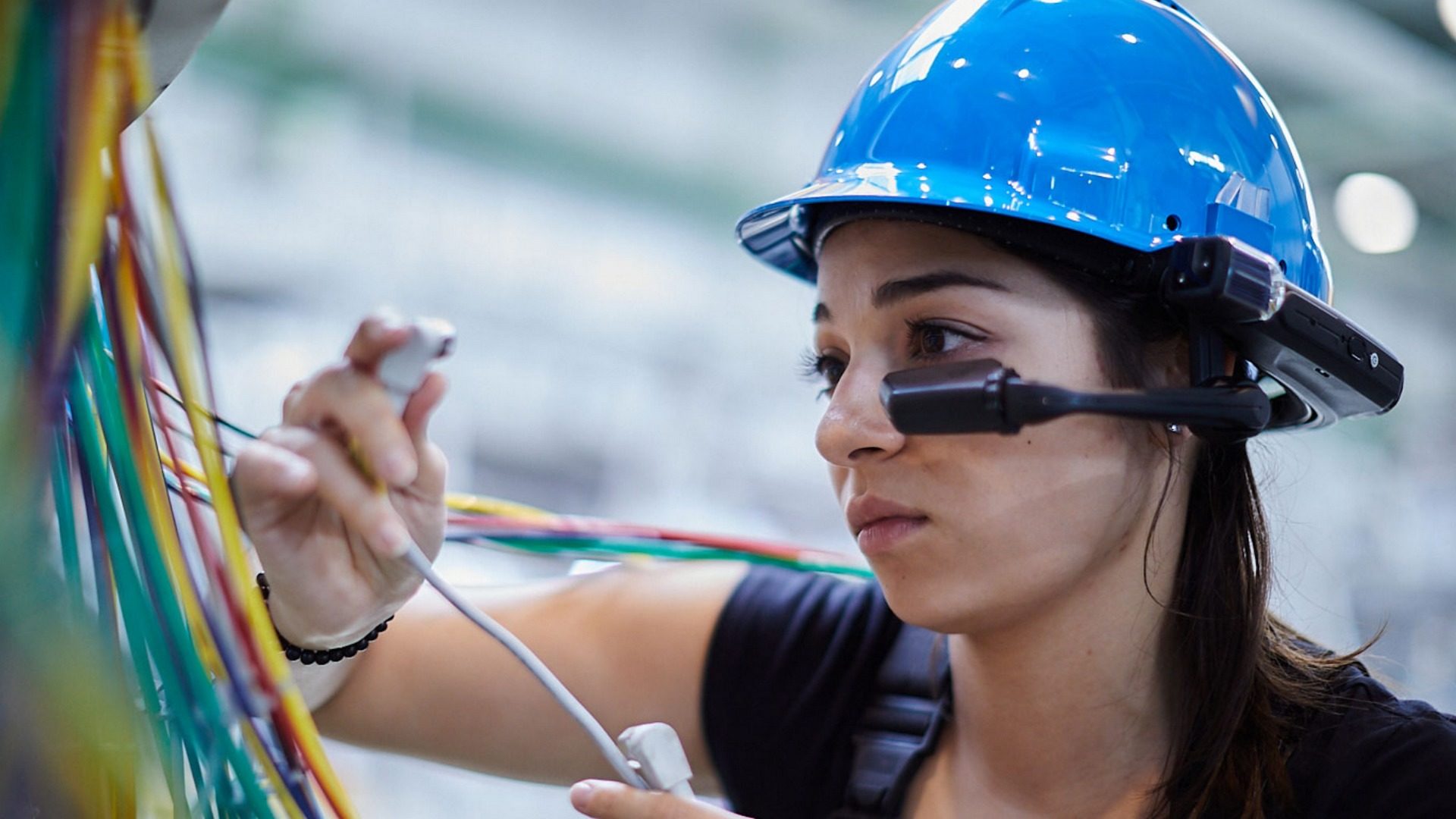 Frau mit blauem Sicherheitshelm und RealWear HMD arbeitet an elektrischen Leitungen