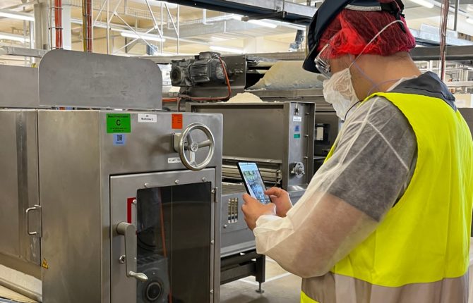 Wartungsperson mit Schutzkleidung prüft über ein Smartphone mit Inspect AR-App eine Maschine in der Lebensmittelproduktion in der Nestlé-Fabrik Wangen
