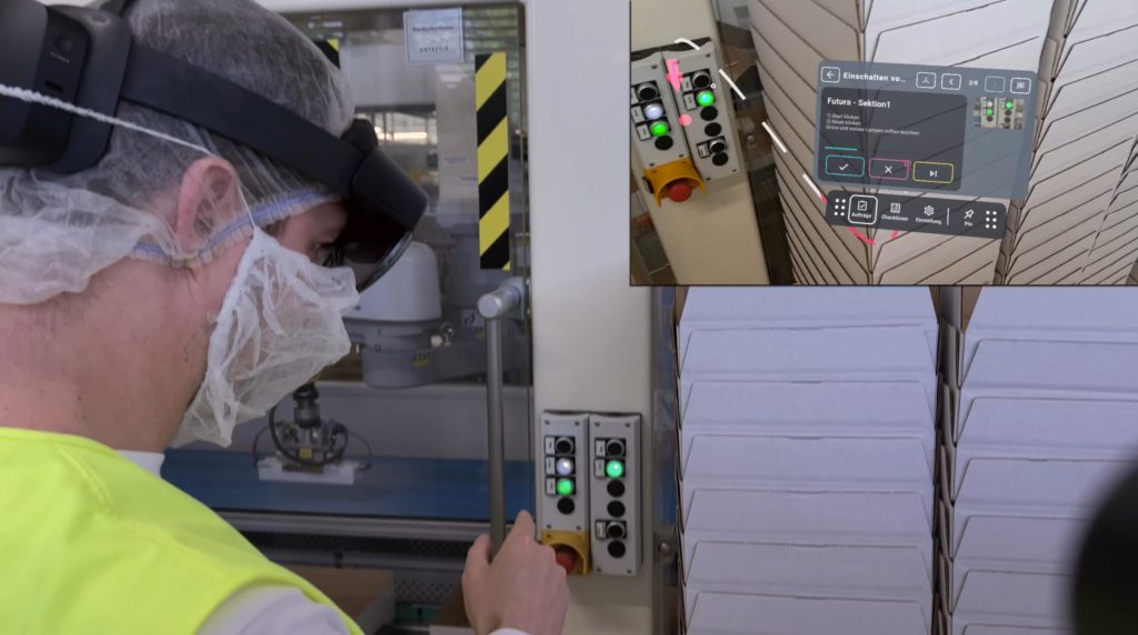 Auszubildender in Schutzkleidung und mit Datenbrille HoloLens 2 auf dem Kopf wird virtuell von der Inspect AR App durch die Funktionsweise einer Produktionsmaschine geführt 